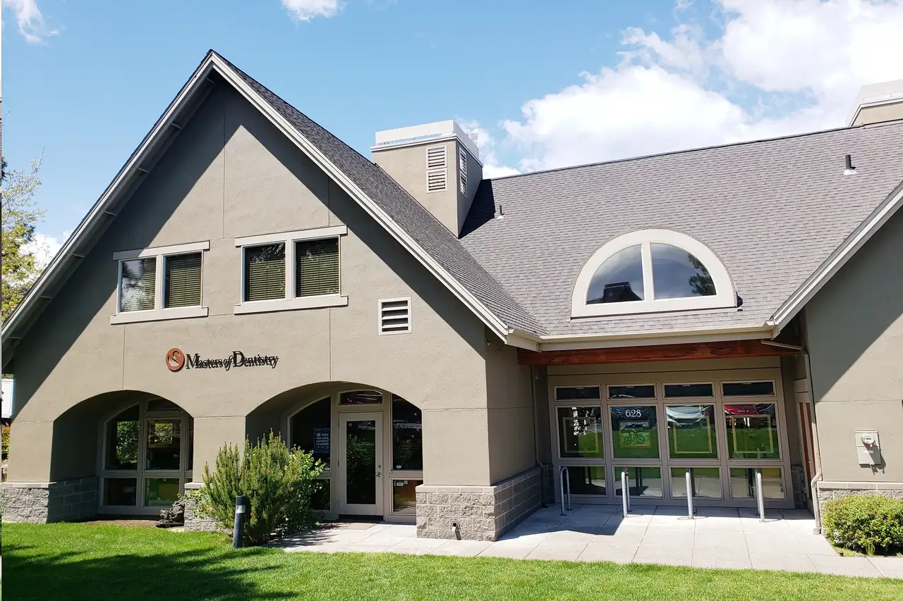 The Masters of Dentistry building at 628 NW York Drive, Bend: grey stucco, a steep gabled roof and the swan sign above the arches.